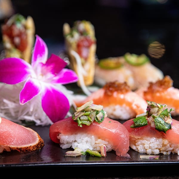 Platter of Blue Wasabi sushi and nigiri, including tuna and salmon, garnished with a purple orchid.