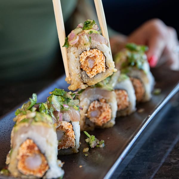 Chopsticks holding a piece of Blue Wasabi sushi roll with shrimp tempura and spicy crab.
