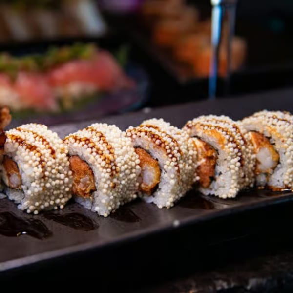 Close-up of Blue Wasabi's sushi roll with crispy rice pearls and a drizzle of sauce.