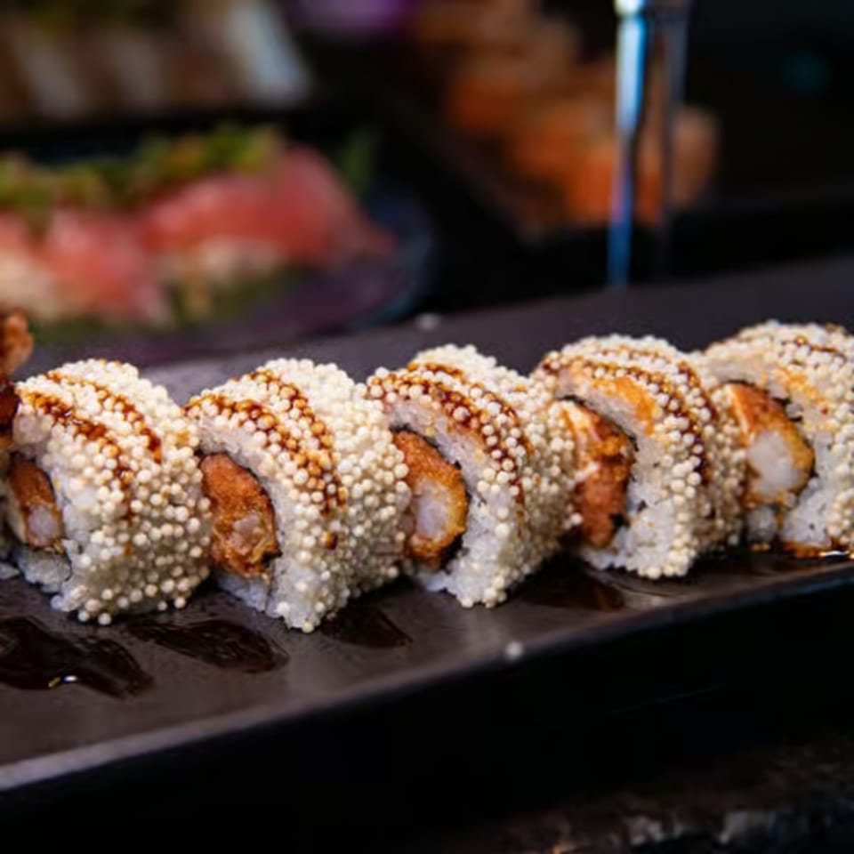 Close-up of Blue Wasabi's sushi roll with crispy rice pearls and a drizzle of sauce.