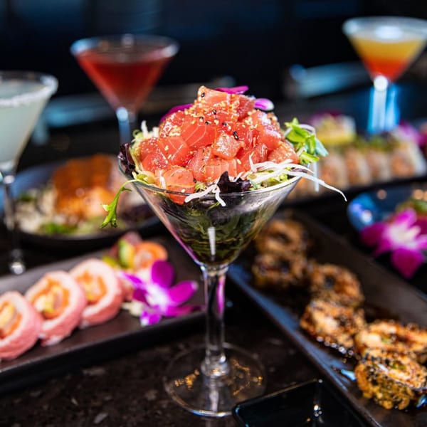 Tuna poke in a martini glass, surrounded by sushi rolls and cocktails at Blue Wasabi.